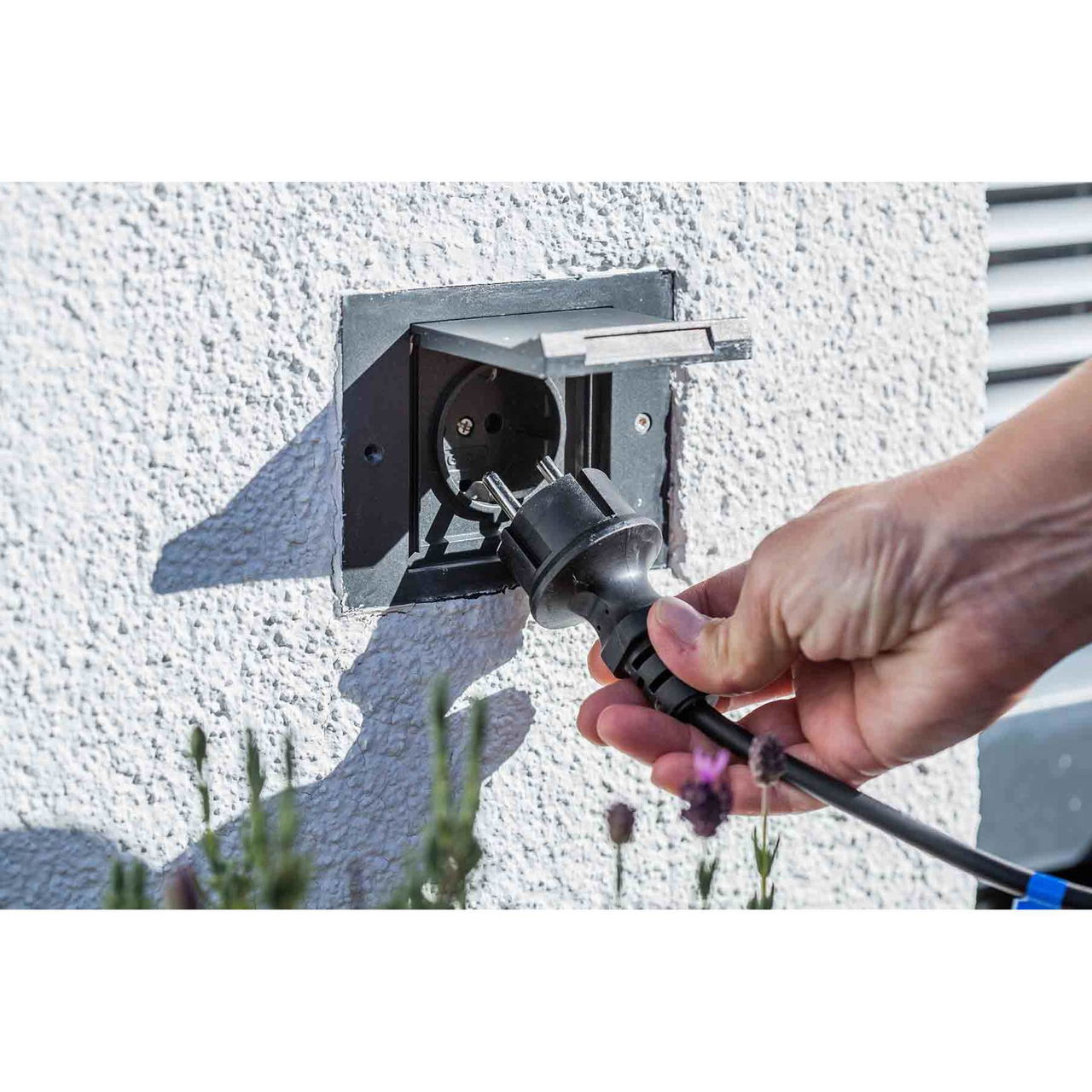 Heissner 015196-00 Rattan Terrassen-Hochteich mit Wasserspiel, schwarz Hand hält Stecker vor Außensteckdose